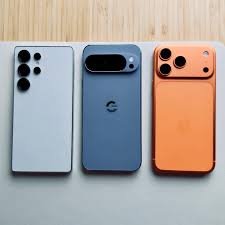 Latest flagship smartphones comparison showing iPhone 17 Pro Max, Samsung Galaxy S25 Ultra, and Google Pixel 10 Pro placed side by side on a wooden surface